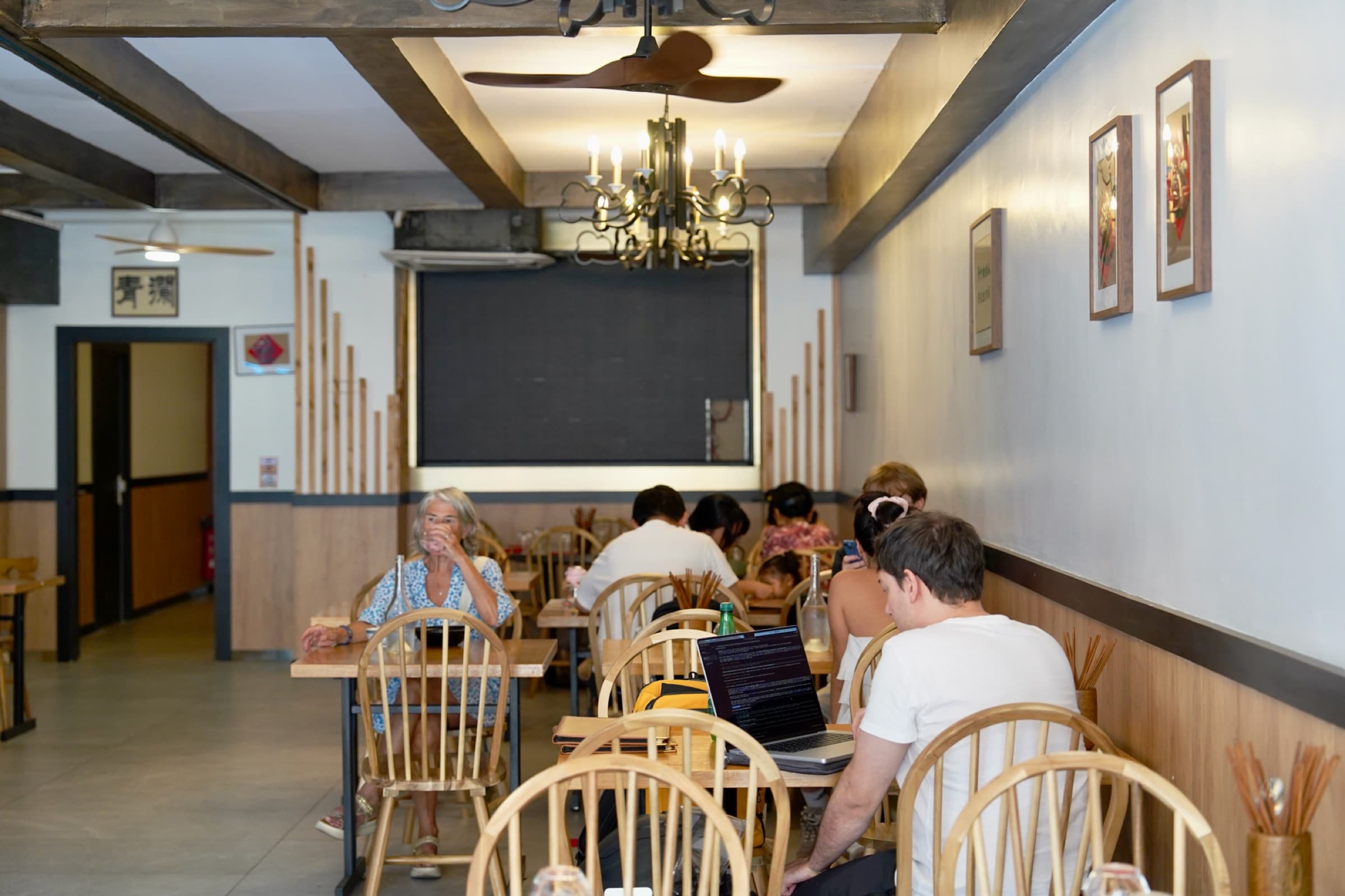 La salle en plein service : tables en bois clair, banquettes et lustre